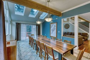 A spacious dining area with a long wooden table and chairs, a staircase with a white railing, and a blue accent wall. - 7BR Hot Tub Lodge • Sleeps 14 • Kodiak (Kodiak)