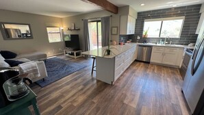 A modern kitchen with a central island, wooden flooring, and a dining area with a sofa and TV. - DesertOasis@ #LambertPark:4BD, Mtn Views, Gym, FREE Heated HOA Pool&Spa, PoolTable, CottonBedding (Tucson)