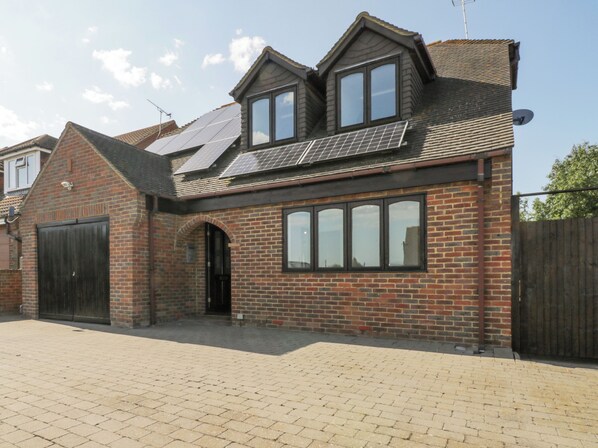 A two-story house with a brick facade, a large garage door, and solar panels on the roof. - Amazing Cottage (Sheerness)