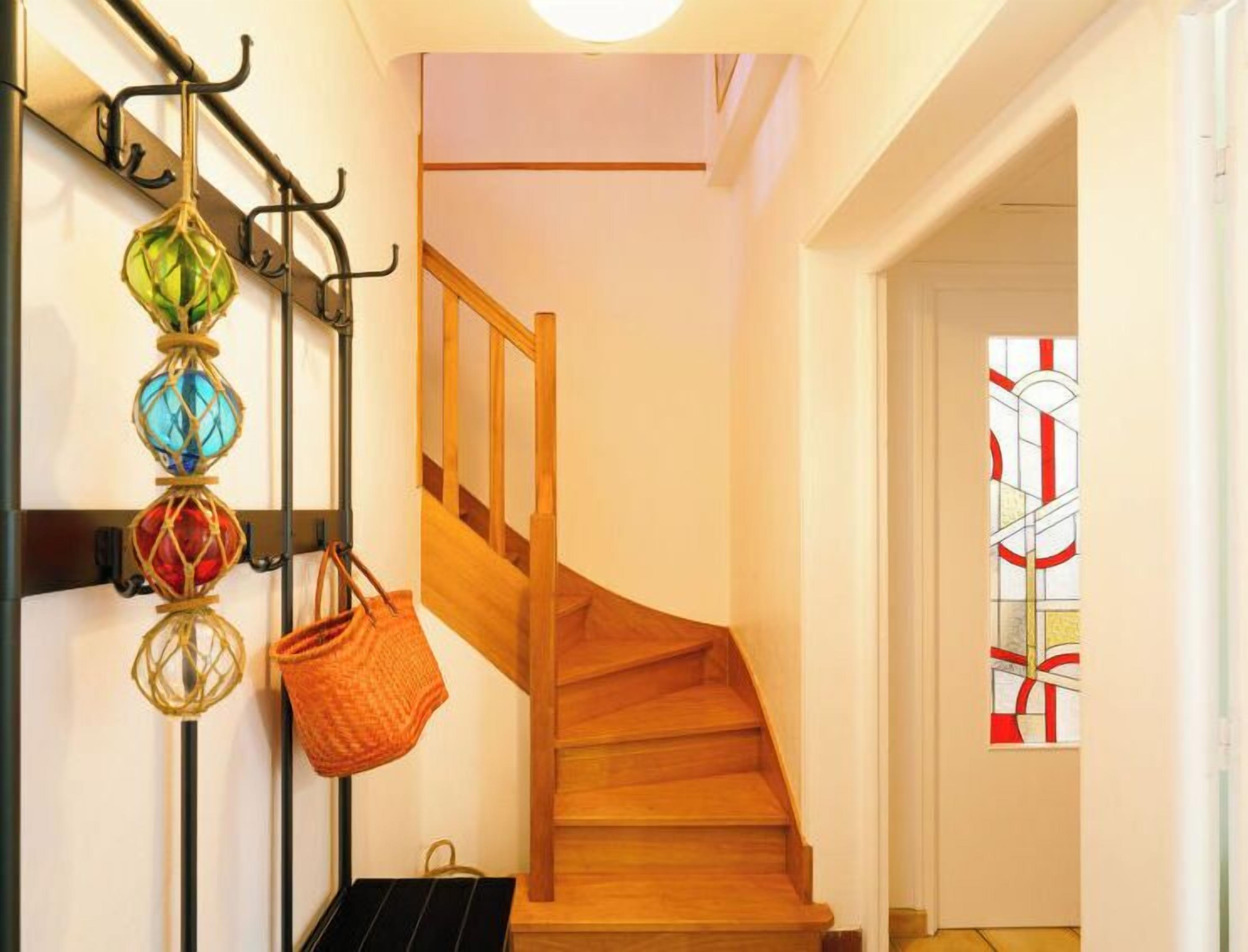 Un escalier en bois avec une rampe, une jardinière suspendue et, au fond, une fenêtre à vitraux.