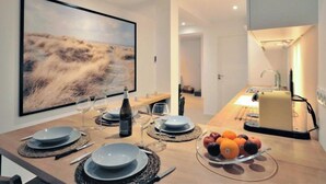 A modern dining area with a large landscape painting, a table set for four with wine glasses and plates, and a fruit bowl on the side. - L'Appart'Mer by Interhome (Plérin)