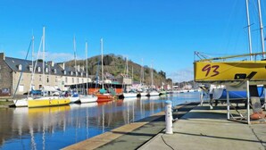 A marina with boats docked, a building with a stone facade, and a hill in the background. - L'Appart'Mer by Interhome (Plérin)