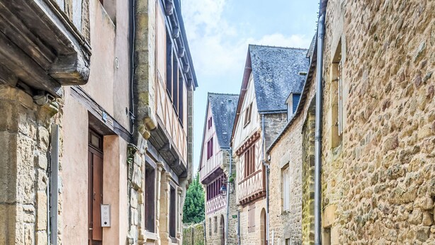 Une ruelle étroite pavée, bordée de bâtiments historiques en pierre, dotés de structures en bois et d’une architecture européenne traditionnelle.