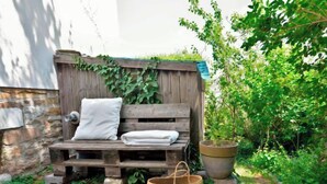 Un espace de détente extérieur au style rustique, avec un banc en bois, un coussin blanc et un panier tressé.