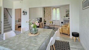 Un espace de repas moderne avec une table dressée pour quatre personnes, une cuisine en arrière-plan et un escalier menant à un autre niveau.
