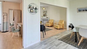 Un salon moderne comprenant un coin repas, une cheminée et une cuisine visible à travers une porte ouverte.