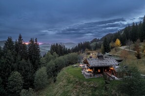 A rustic cabin with a stone roof, surrounded by dense forest and a view of distant mountains. - Buccara Zwischenbachalm  (Westendorf)