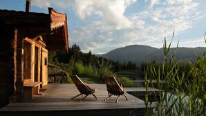 Una cabaña de madera con un porche, dos sillones de descanso y vistas a un lago y montañas.