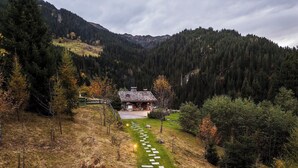 Una cabaña rústica de montaña con un sendero de piedra que conduce a la entrada, rodeada de un bosque denso y colinas.