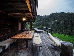 A wooden deck with a table and lounge chairs, overlooking a forested mountain.