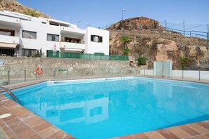 A swimming pool with a clear blue water, surrounded by a stone wall and a white building with balconies. - Vacation Home 'Suite Deluxe Puerto Rico B' with Shared Pool, Wi-Fi and Air Conditioning (Puerto Rico)