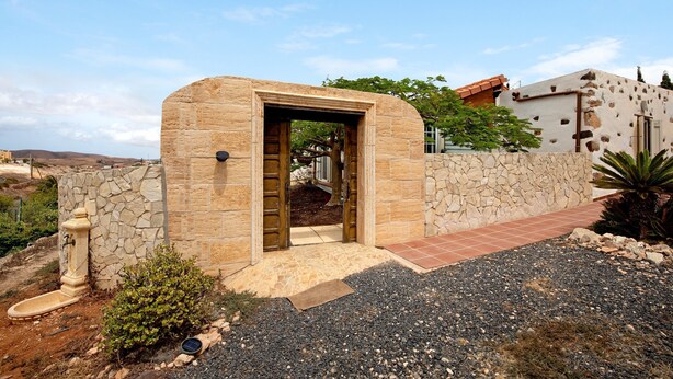 Una entrada de piedra con puerta, un pequeño jardín y vistas del paisaje circundante.