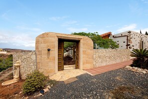 Una entrada de piedra con puerta, un pequeño jardín y vistas del paisaje circundante.