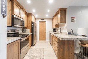 Une cuisine moderne avec des meubles en bois, des appareils électroménagers en acier inoxydable, des plans de travail en granit et un four encastré.