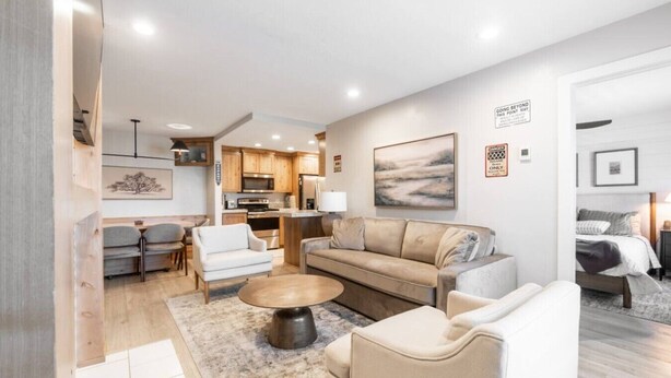 A modern living room with a sofa, armchairs, and a coffee table. There is a kitchen area with wooden cabinets and a dining table. - Designer Ski-In / Ski-Out Condominium At Brian Heads Copper Chase (Brian Head)