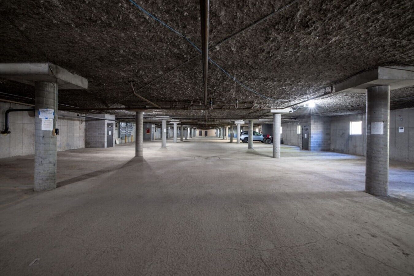 Un grand parking couvert, à ciel ouvert, avec des piliers en béton et un plafond très haut.
