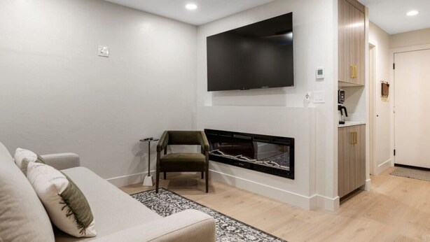 Una sala de estar moderna con un televisor de pantalla plana sobre una chimenea, un sofá y un sillón.