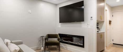 A modern living room with a flat-screen TV mounted above a fireplace, a sofa, and a chair.