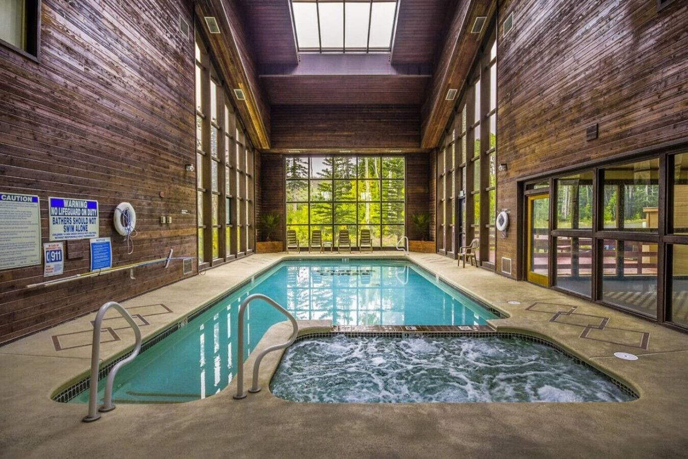 Une piscine intérieure avec un jacuzzi, des murs en bois et de grandes fenêtres.