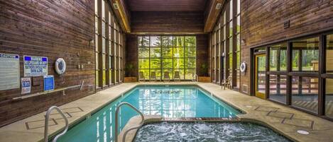 Piscina interna com hidromassagem, paredes de madeira e grandes janelas.