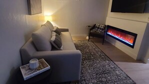 A modern living room with a sofa, a side table, a fireplace, a ceiling fan, and a mounted TV. - Designer Ski-In / Ski-Out Condominium at the top of Brian Heads Navajo Lift (Brian Head)