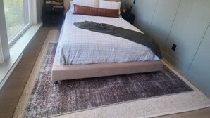 A bedroom with a large bed, a nightstand, a wall-mounted lamp, and a window with a view of trees. - Designer Ski-In / Ski-Out Condominium at the top of Brian Heads Navajo Lift (Brian Head)