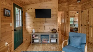 Interno di una baita in legno con una TV a muro, un caminetto, una porta verde e una poltrona blu.