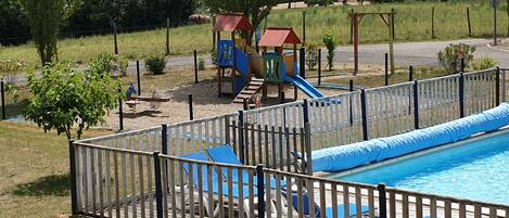 A fenced swimming pool area with a slide and play structures.