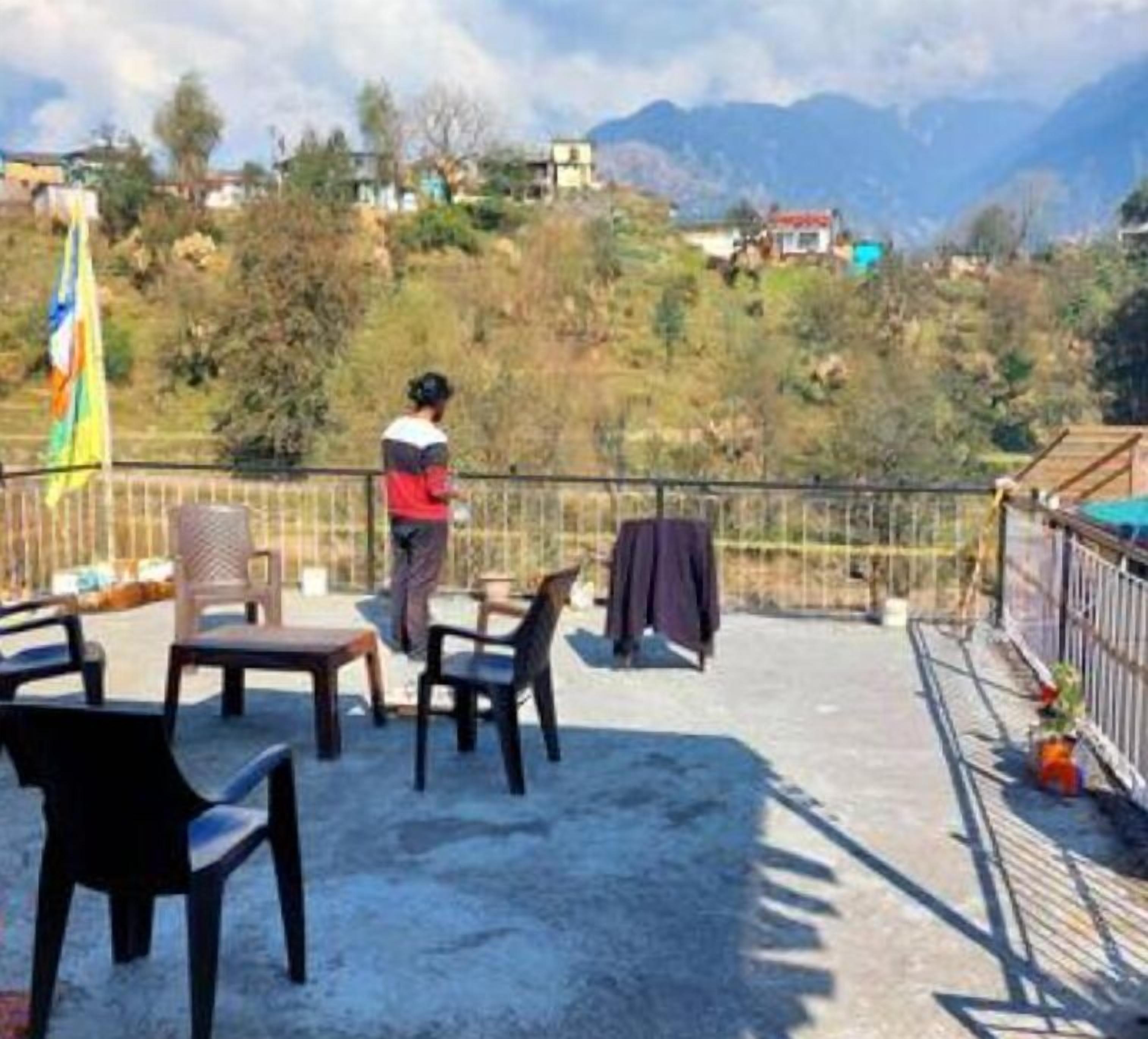 A terrace with chairs and a table, overlooking a mountainous landscape with houses in the background.