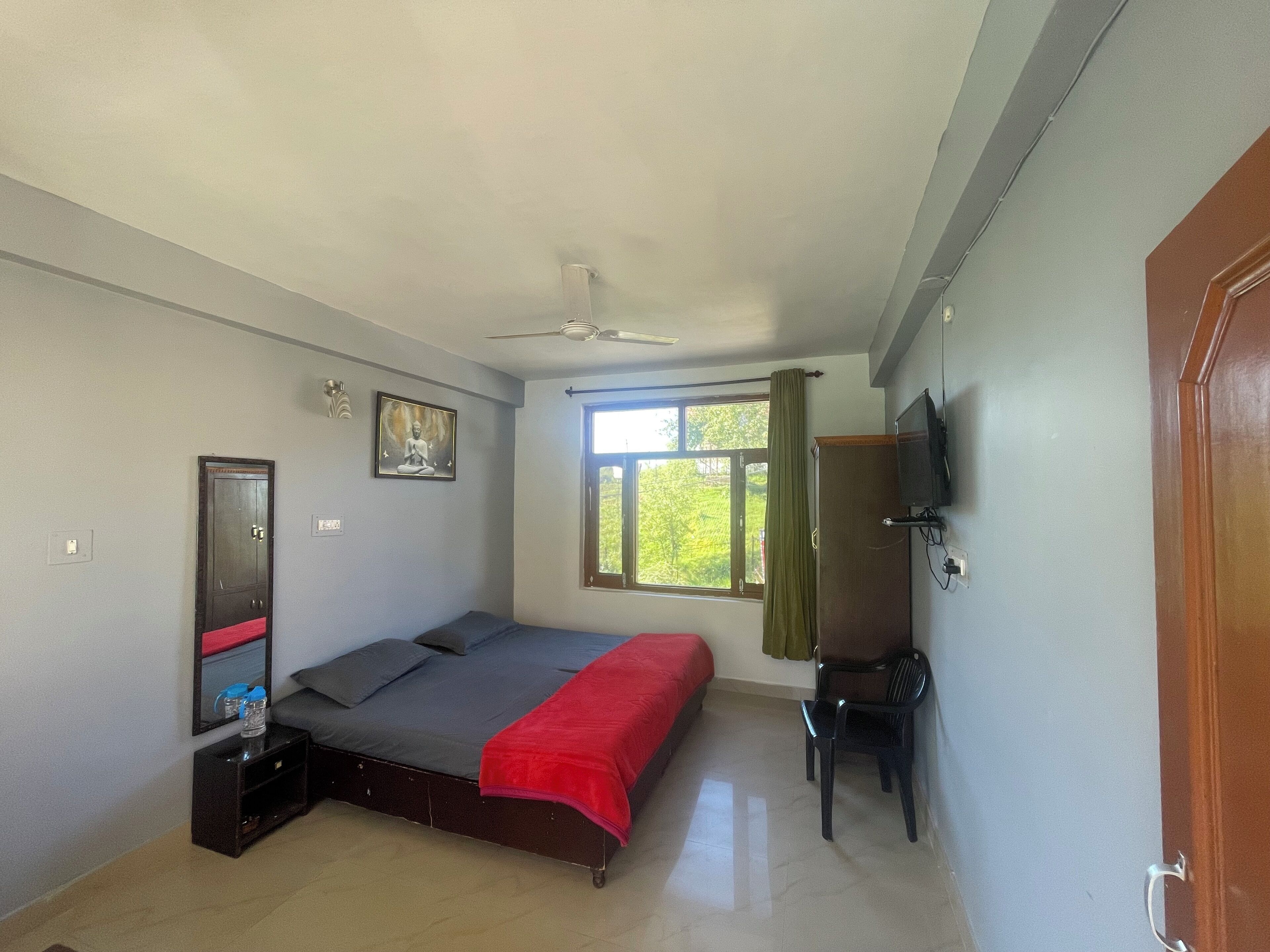 A bedroom with a bed, a television, a window with curtains, a ceiling fan, and a door.
