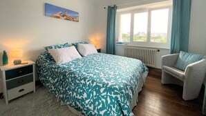 A bedroom with a bed, a chair, a nightstand, a lamp, a window with curtains, and a painting on the wall. - House in Perros-Guirec with WiFi 550m from Trestraou Beach (Perros-Guirec)