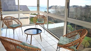 A sunroom with large windows, wicker furniture, and a view of the sea. - House in Perros-Guirec with WiFi 550m from Trestraou Beach (Perros-Guirec)