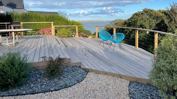 A wooden deck with a view of the sea, surrounded by greenery and a wooden fence. - House in Perros-Guirec with WiFi 550m from Trestraou Beach (Perros-Guirec)