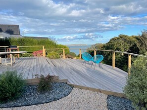 Um deck de madeira com vista para o mar, cercado por vegetação e um cercado de madeira.