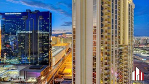 A high-rise hotel with multiple floors and balconies, surrounded by a cityscape with other buildings and a clear sky. - MGM Signature-30-705 F1 Track & Strip View Balcony (Las Vegas)