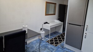 Une chambre d’hôtel compacte, dotée d’un bureau, d’une chaise, d’une armoire blanche et d’une salle de bain avec un miroir et un lavabo.