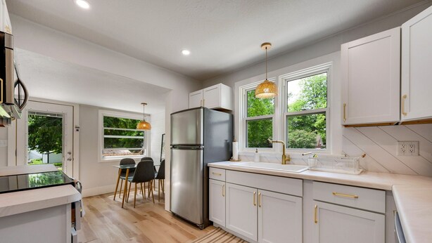 A modern kitchen with white cabinets, a stainless steel refrigerator, and a dining area with a table and chairs. - Teresa's Cottage - Walkable to downtown Sturgeon Bay (Sturgeon Bay)