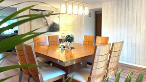 A dining area with a wooden table and chairs, a pendant light, and a plant on the table.