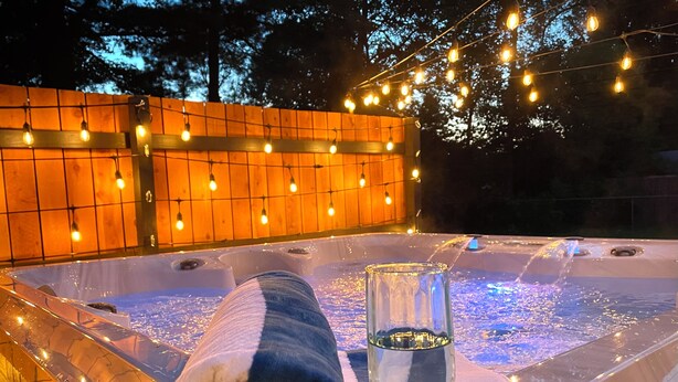 A hot tub with a glass of water, a towel, and string lights.