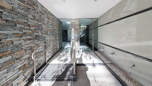 Un pasillo interior moderno con una pared de piedra, puertas de vidrio y una barandilla de metal.