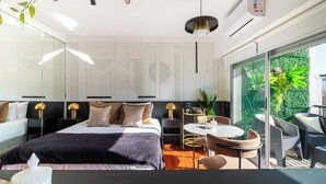 Una habitación de hotel moderna con una cama grande, un área de comedor y un balcón con plantas.
