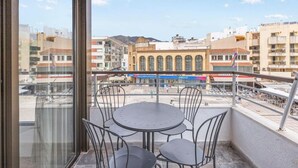 Un balcón con mesa y sillas, con vista a un paisaje urbano que incluye edificios y una montaña al fondo.