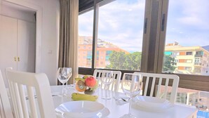 Una mesa de comedor dispuesta con platos, cubiertos y copas de vino, con un frutero y plátanos sobre la mesa.