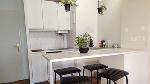 A modern kitchen with white cabinetry, a white countertop, and three black bar stools.