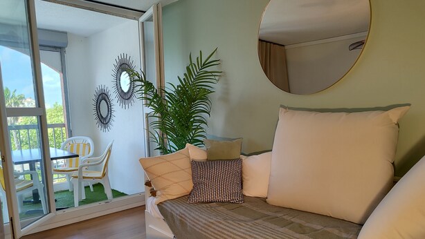 A room with a sofa, a mirror, a potted plant, and a view of an outdoor area with chairs and a table.