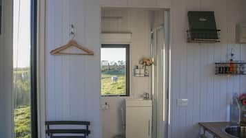 A compact kitchen with a window view of a green field, a hanging wooden hanger, a small sink, and a built-in stove.