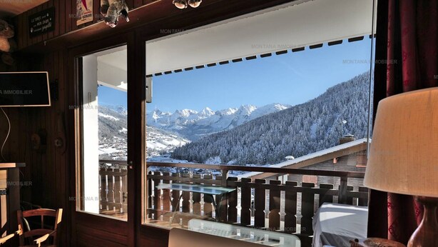 A room with a wooden interior, a view of snow-covered mountains, and a glass door leading to an outdoor balcony.