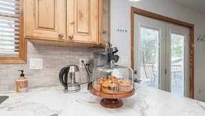 A kitchen with wooden cabinets, a marble countertop, a coffee maker, a glass display case with muffins, and a bottle of hand soap. - Grand Palace Cottage Escape (Sioux Falls)