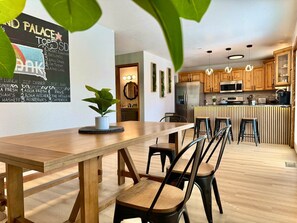 A modern kitchen with wooden cabinets, a central island with stools, and a dining area with a long table and chairs.