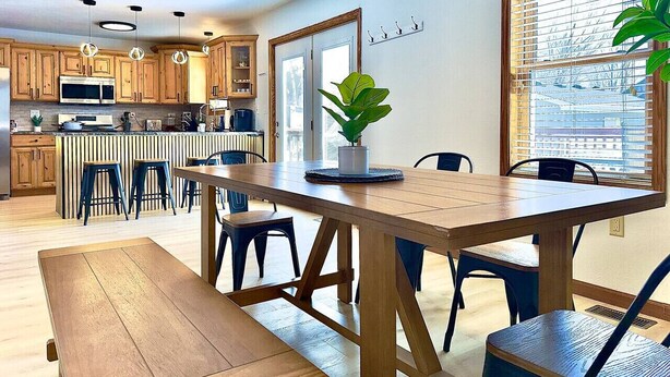 A modern kitchen with wooden cabinets, a central island, and a dining area with a wooden table and chairs. - Grand Palace Cottage Escape (Sioux Falls)